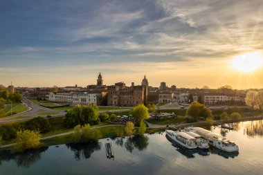 Mantua İtalya 'nın romantik günbatımı manzarası tarihi gökyüzü Castello di San Giorgio nehir kenarı parkı ve demirlemiş tekneler Mincio Nehri manzaralı seyahat manzarasına yansıyor.