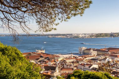 Lizbon şehir merkezinin panoramik manzarası Praa do Comercio Tagus Nehri ve güneşli bir günde ağaçların çerçevelediği kırmızı çatılar