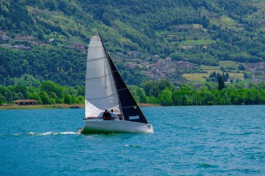 Iseo Gölü 'nde seyir halinde olan yelkenli İtalya' da yemyeşil tepeler ve arka planda yamaçlarda köyler var. Yaz macerası ve sakin açık hava havası