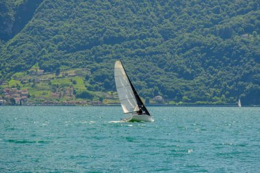 Iseo Gölü 'nde seyir halinde olan yelkenli İtalya' da yemyeşil tepeler ve dağ köyleri arka planda yaz macerası ve sakin açık hava havası