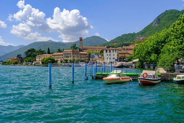 Lovere 'nin Iseo Gölü' ndeki manzarası, Lombardy, İtalya. Renkli tekneler, tarihi binalar ve parlak bir gökyüzünün altındaki dağlar. Seyahat ve turizm temaları için ideal.