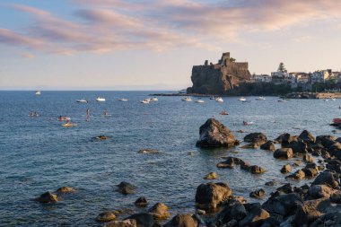 Günbatımı manzaralı Acicastello 'nun Norman kalesi lav kayalıkları üzerinde seyahat kültürü tarihi ve Akdeniz yaşam tarzı kavramları için balıkçı tekneleri limanında.