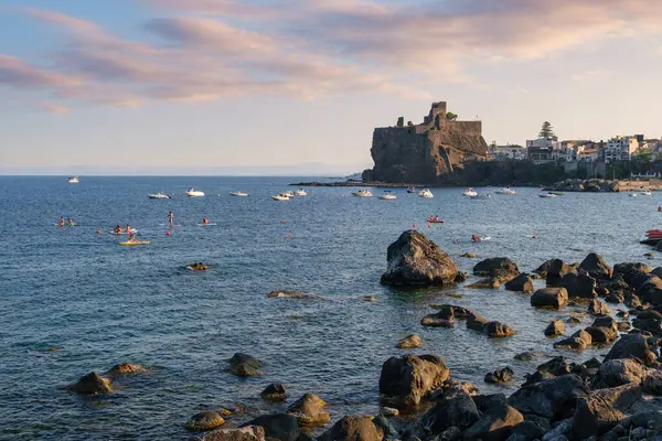 Günbatımı manzaralı Acicastello 'nun Norman kalesi lav kayalıkları üzerinde seyahat kültürü tarihi ve Akdeniz yaşam tarzı kavramları için balıkçı tekneleri limanında.