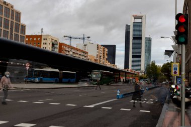 Şehre. Plaza Castilla yolu araçlar, arabalar, motosikletler, otobüsler ve toplu taşıma araçlarıyla dolu, Madrid 'de bulutlu bir günde arka planda gökdelenler var. Zebra geçidinden geçen insanlar.