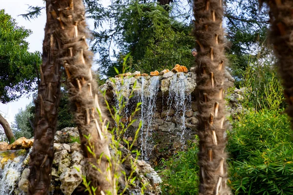 Waterfall. Waterfall in a park in Madrid. Artificial Mountain of Buen Retiro, called Mountain of the Cats. Dark stone background surrounded by green vegetation and plants and leaves. Autumn colors.