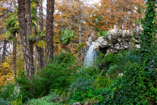 Waterfall. Waterfall in a park in Madrid. Artificial Mountain of Buen Retiro, called Mountain of the Cats. Dark stone background surrounded by green vegetation and plants and leaves. Autumn colors.