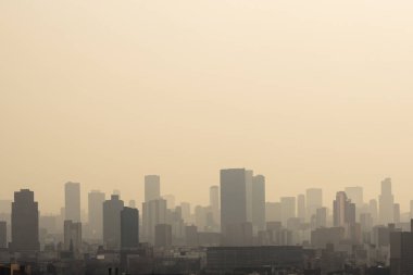 Haze. Gökyüzü puslu ve bulutlu. Sisli bir sabahta yüksek binaların silueti. Şiddetli hava kirliliği, bulanıklığı ve kötü görüş mesafesi şehirdeki yüksek binaları net bir şekilde görmemi zorlaştırıyor..