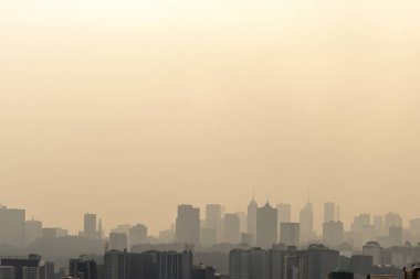 Haze. Gökyüzü puslu ve bulutlu. Sisli bir sabahta yüksek binaların silueti. Şiddetli hava kirliliği, bulanıklığı ve kötü görüş mesafesi şehirdeki yüksek binaları net bir şekilde görmemi zorlaştırıyor..