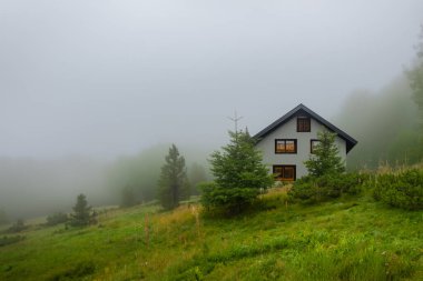 Dağlarda ıssız bir ev, güzel tipik bir kuzey Avrupa evi, yemyeşil, sisli bir manzara. Yeşil çayırları ve dağlarda evi olan güzel yaz manzarası.