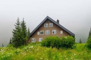 Dağlarda ıssız bir ev, güzel tipik bir kuzey Avrupa evi, yemyeşil, sisli bir manzara. Yeşil çayırları ve dağlarda evi olan güzel yaz manzarası.