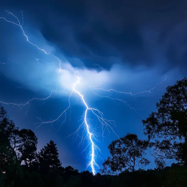 stock image Lightning. Lightning strike. Spectacular night view of a lightning bolt streaking across the dark blue sky. Lightning and thunder and flashes. Clouds and silhouettes of trees are visible.