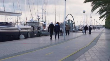 Palma de Mallorca, Spain; january 06 2023: A promenade with pedestrians, and luxury yachts and sailboats moored in the harbor of the tourist city of Palma de Mallorca at sunset. Spain