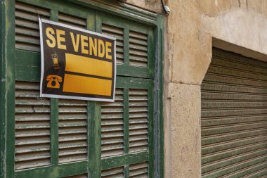 Terk edilmiş yeşil bir Mallorcan kepengi olan ve İspanyolca satılık tabelası olan bir evin kapısı. İspanya 'daki nüfusun konut sorununun resmi. Mallorca