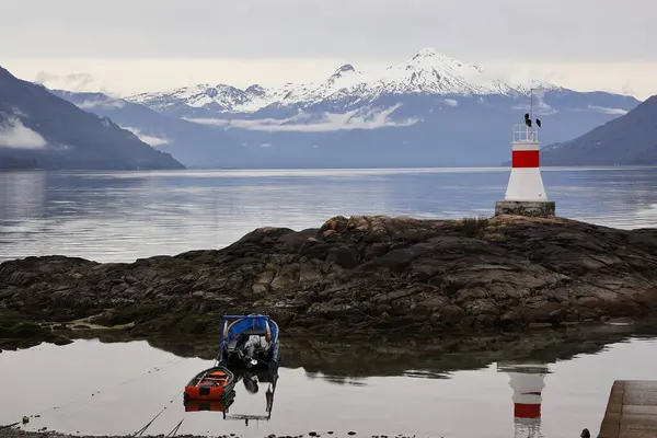 Şili 'nin güneyindeki fiyort bir ışık evi ve karlı dağları yansıtıyor. Fotoğraf bulutlu bir günde Cocham 'da çekildi..