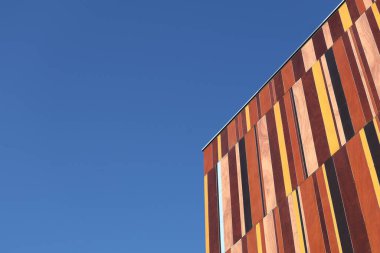 Mavi gökyüzüne karşı çok renkli ahşap panelleri olan bir binanın kenarında. Sol tarafta boşluk yok..