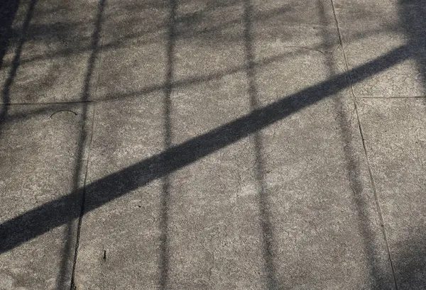 Çitin çapraz gölgesi ya da gündüz vakti beton bir kaldırıma atılan korkuluklar. Minimalist kompozisyon, kentsel arkaplan veya soyut kavram.