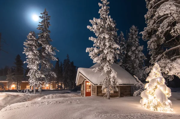 Outdoor winter and Christmas scene with wooden cabin in the woods. Winter forest landscape at full moon, Finland, Lapland.