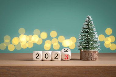 Mini noel ağacı ve ahşap bloklar 2022 yılının yeşil arka planda 2023 yılına geçiyorlar. Yeni yıl konsepti.