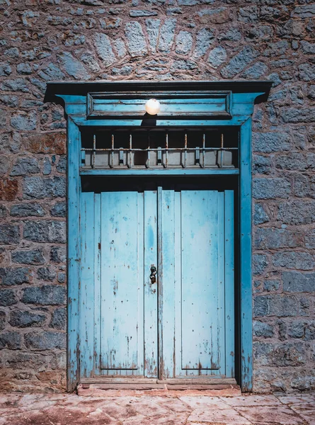 Old blue wooden door lit by a lamp above. Architecture in Hydra town, Greece.