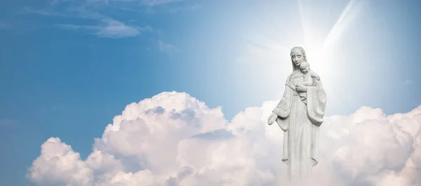 Mother Mary and Baby Jesus Statue against blue sky with white clouds background.