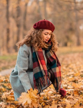 Güzel gözleri olan, şık gri bir ceket giyen ve parkta ağaçların yanında oturan kıvırcık, neşeli bir kız. Sonbahar zamanı. Portre.