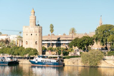 Seville, İspanya; 18 Kasım 2023: Guadalquivir Nehri 'ndeki kulenin önüne yanaşmış bir turist teknesiyle Torre del Oro manzarası.