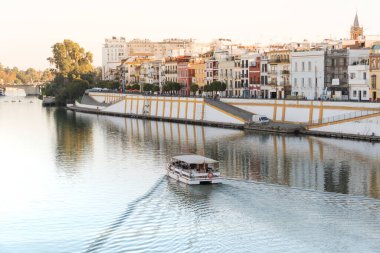 Seville, İspanya; 18 Kasım 2023: Sevilla 'nın (Endülüs, İspanya) ünlü Betis Caddesi' nin önündeki Guadalquivir Nehri 'ndeki turist teknesi. Sevilla 'daki renkli binalar.