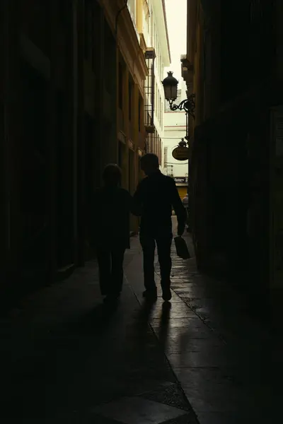 Jerez de la Frontera, İspanya; 17 Nisan 2024: Karanlık bir sokakta yürüyen yaşlı bir çiftin silueti.