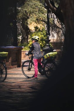 Jerez de la Frontera, İspanya; 19 Nisan 2024: Parkta bisikletinin yanında kask ve aksesuar takan kadın. Bir şehir parkında bisiklet gezgini.