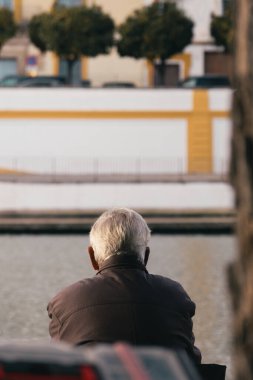 Sevilla 'daki Guadalquivir Nehri' nin önünde oturan yaşlı adam. Guadalquivir Nehri 'ni gözetleyen bir adamın arka görüntüsü..