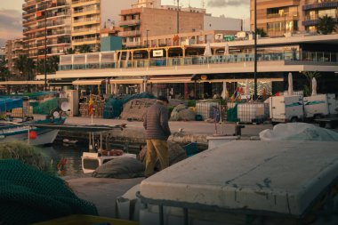 Santa Pola, İspanya; 27 Aralık 2024: Yaşlı bir adam balıkçı ağları ve balıkçı tekneleriyle çevrili bir balıkçı limanında yürüyor.