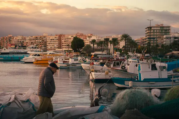 Santa Pola, İspanya; 27 Aralık 2024: Yaşlı bir adam balıkçı ağları ve balıkçı tekneleriyle çevrili bir balıkçı limanında yürüyor.