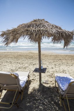 Şemsiye ve iki güneş şezlongu deniz kenarındaki ilk hatta.