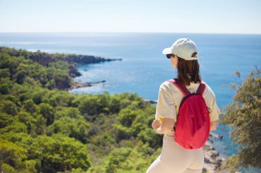 Pembe sırt çantalı genç kadın yürüyüş sırasında Akdeniz kıyılarına karşı duruyor..