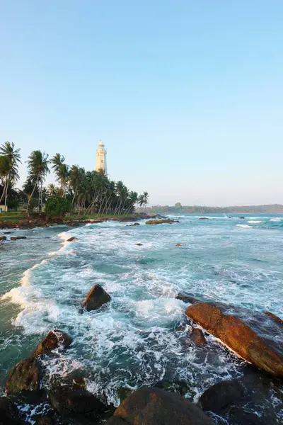 stock image Dondra, Sri Lanka - 23.01.2023. A white Dondra Head Lighthouse among the green palms on the rocky oceanic coast. Hidden gem of Sri