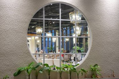 Yeşil, modern bir kafeye açılan beyaz, yuvarlak bir pencere. Beyaz duvar ve bitkiler ile temiz iç tasarım