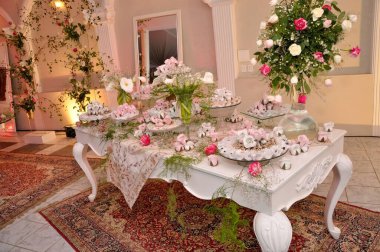 Çok güzel dekore edilmiş bir tatlı masası bir sürü tatlı ikram. Pastel renkli çiçekler ve zarif dekorlarla süslenmiş. Karmaşık halılar ve gür yeşilliklerle dolu sofistike bir ortamda..