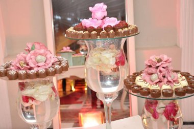 Aynalı yüzeylere zarif bir şekilde yerleştirilmiş, pembe ve beyaz suni çiçeklerle süslenmiş, lüks ve şenlikli bir atmosfer yaratan çikolataların sofistike bir sunumu..