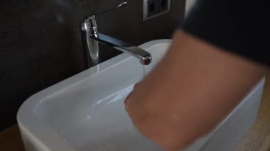 Modern lavaboda ellerini yıkayan adam - kişisel hijyen konsepti. Modern bir banyo lavabosunda ellerini akan suyun altında yıkayan bir adamın videosu. Kişisel hijyen, sağlık, virüs önleme ve