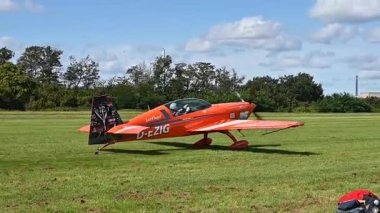 Leverkusen, Almanya - 26 Ağustos 2023: Flugfest Leverkusen 'de yeşil çimlere park edilmiş turuncu aerobatik uçak D-EZIG, havacılık kültürü ve açık hava etkinliklerini vurguladı. Yüksek kaliteli FullHD görüntüler