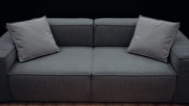 同じ色のクッションを持つシンプルなグレーのソファは 黒の背景にゆっくりと撮影しました 4Kビデオ ロイヤリティフリーのストック動画