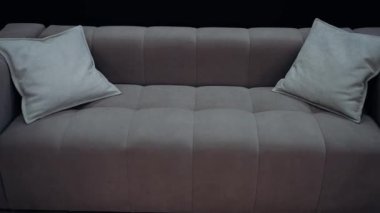 Orta bej yastıklı kahverengi bir kanepe, ofiste siyah bir arka planda ağır çekimde çekilmiş. 4k video