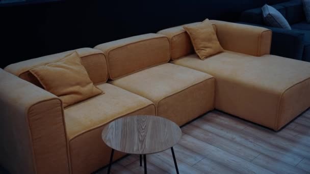 色んな色のソファがあります 中央には 小さな木製のテーブルの横に装飾的な枕を持つ黄色の茶色のソファ 黒の背景 4Kビデオ ロイヤリティフリーのストック動画