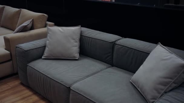 家具店で撮影した2つの枕を持つグレーのソファは 背景に快適な茶色のソファがあります 4Kビデオ ストック映像