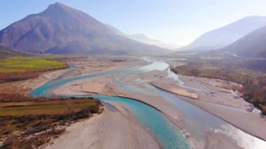 Colorful river Vjosa landscape with turquoise water streaming on pebbles, mountains and blue sky background.