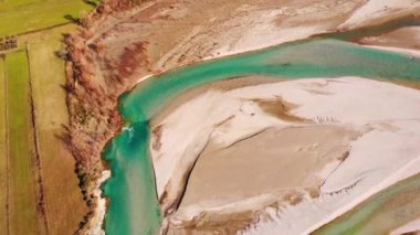Colorful river Vjosa landscape with turquoise water streaming on pebbles, mountains and blue sky background.