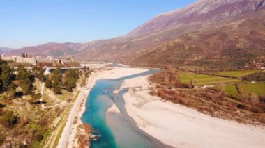 Colorful river Vjosa landscape with turquoise water streaming on pebbles, mountains and blue sky background.