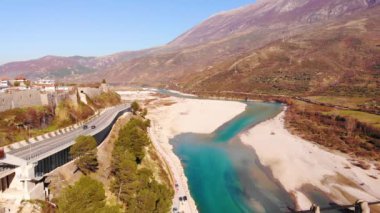 Colorful river Vjosa landscape with turquoise water streaming on pebbles, mountains and blue sky background.