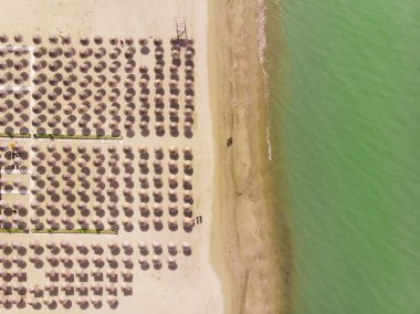 Yukarıdan temiz mavi suyu olan güzel bir kumsalın manzarası. Sahilde çiğ kumsal şemsiyeleri. Yaz mevsimi konsepti.