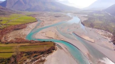 Colorful river Vjosa landscape with turquoise water streaming on pebbles, mountains and blue sky background.